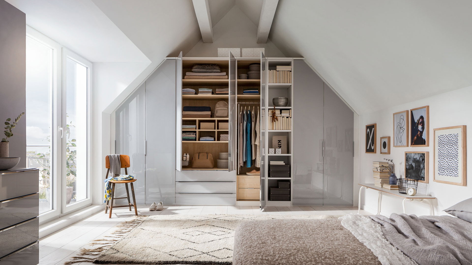 Moderner Kleiderschrank mit offenen Fächern und Stauraum unter einer Dachschräge in einem hellen Schlafzimmer.