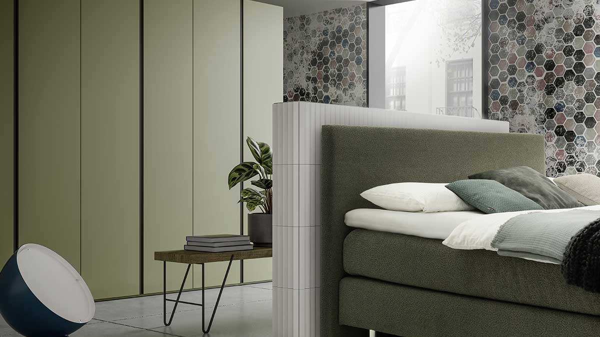 Schlafzimmer mit grünem Polsterbett vor Raumtrenner und grüner Schrankwand