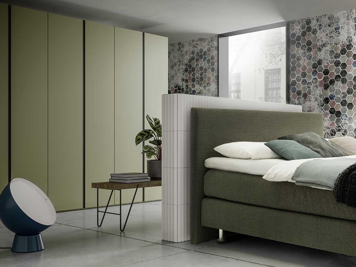 Schlafzimmer mit grünem Polsterbett vor Raumtrenner und grüner Schrankwand