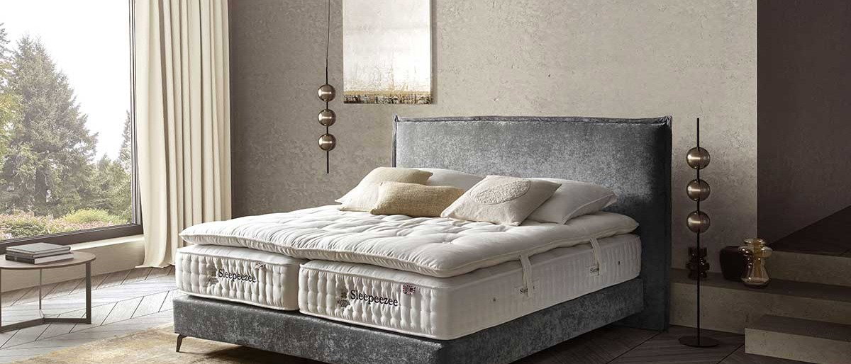 Schlafzimmer mit Polsterbett, hellbraunem Teppich und beigen Vorh&auml;ngen