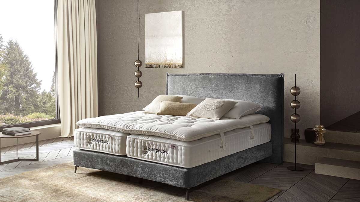 Schlafzimmer mit Polsterbett, hellbraunem Teppich und beigen Vorhängen