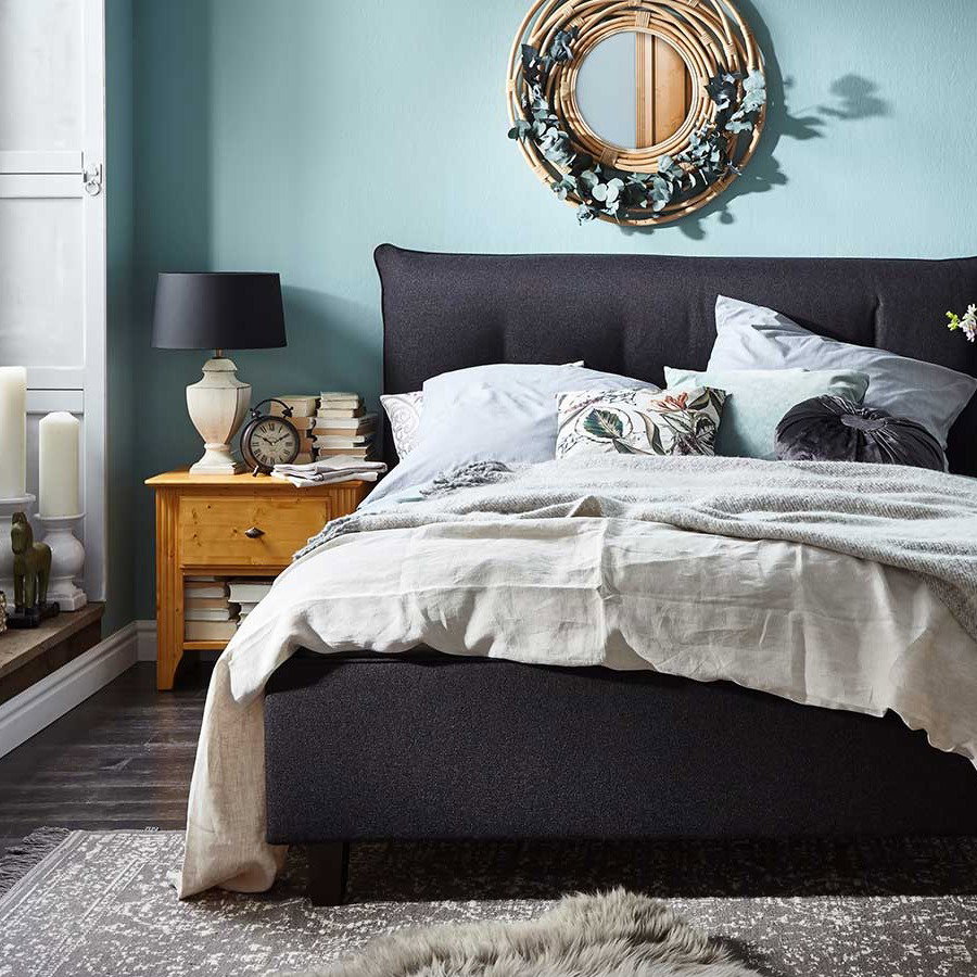 Schlafzimmer mit anthrazit Polsterbett vor hellblauer Wand