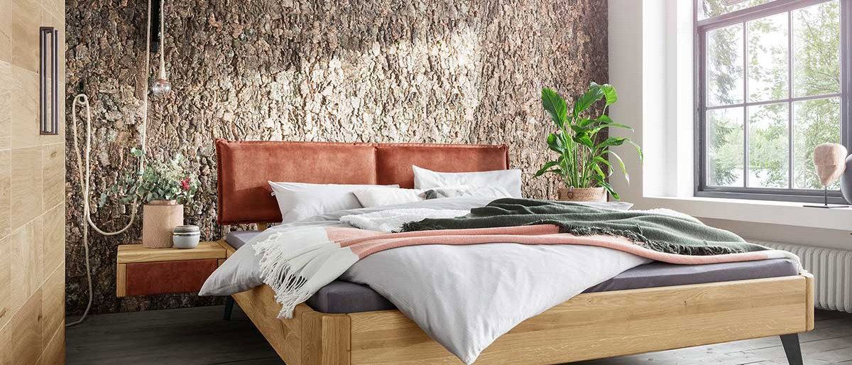 Doppelbett aus Holz vor Natursteinwand