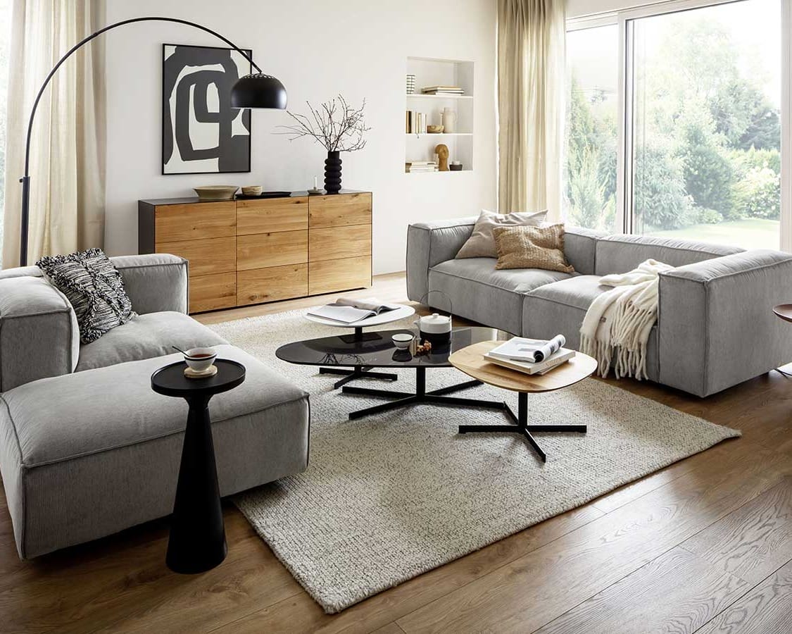 Gemütliches Wohnzimmer im Spätsommer, Wohnzimmer mit hellgrauen Polstermöbeln, naturfarbenem Sideboard und schwarzen Dekoartikeln