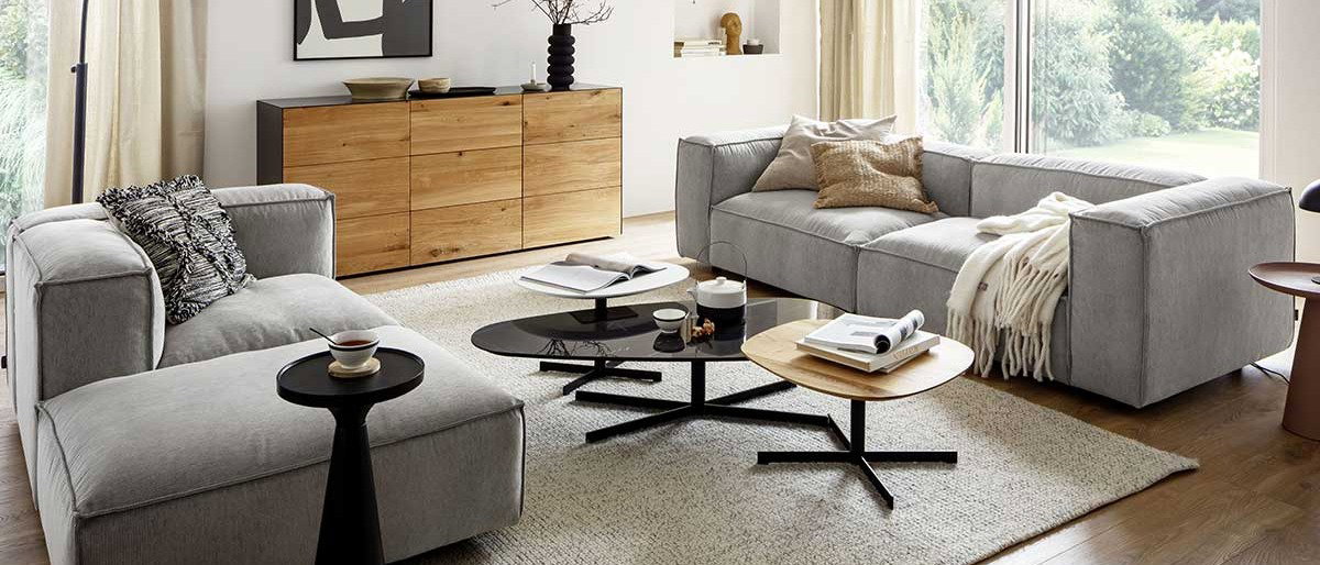 Gemütliches Wohnzimmer im Spätsommer, Wohnzimmer mit hellgrauen Polstermöbeln, naturfarbenem Sideboard und schwarzen Dekoartikeln