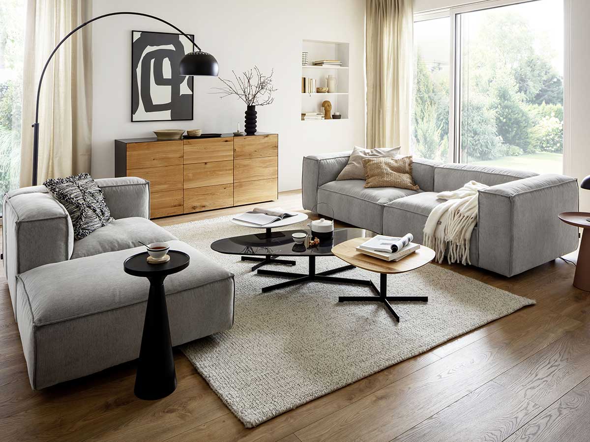 Gemütliches Wohnzimmer im Spätsommer, Wohnzimmer mit hellgrauen Polstermöbeln, naturfarbenem Sideboard und schwarzen Dekoartikeln