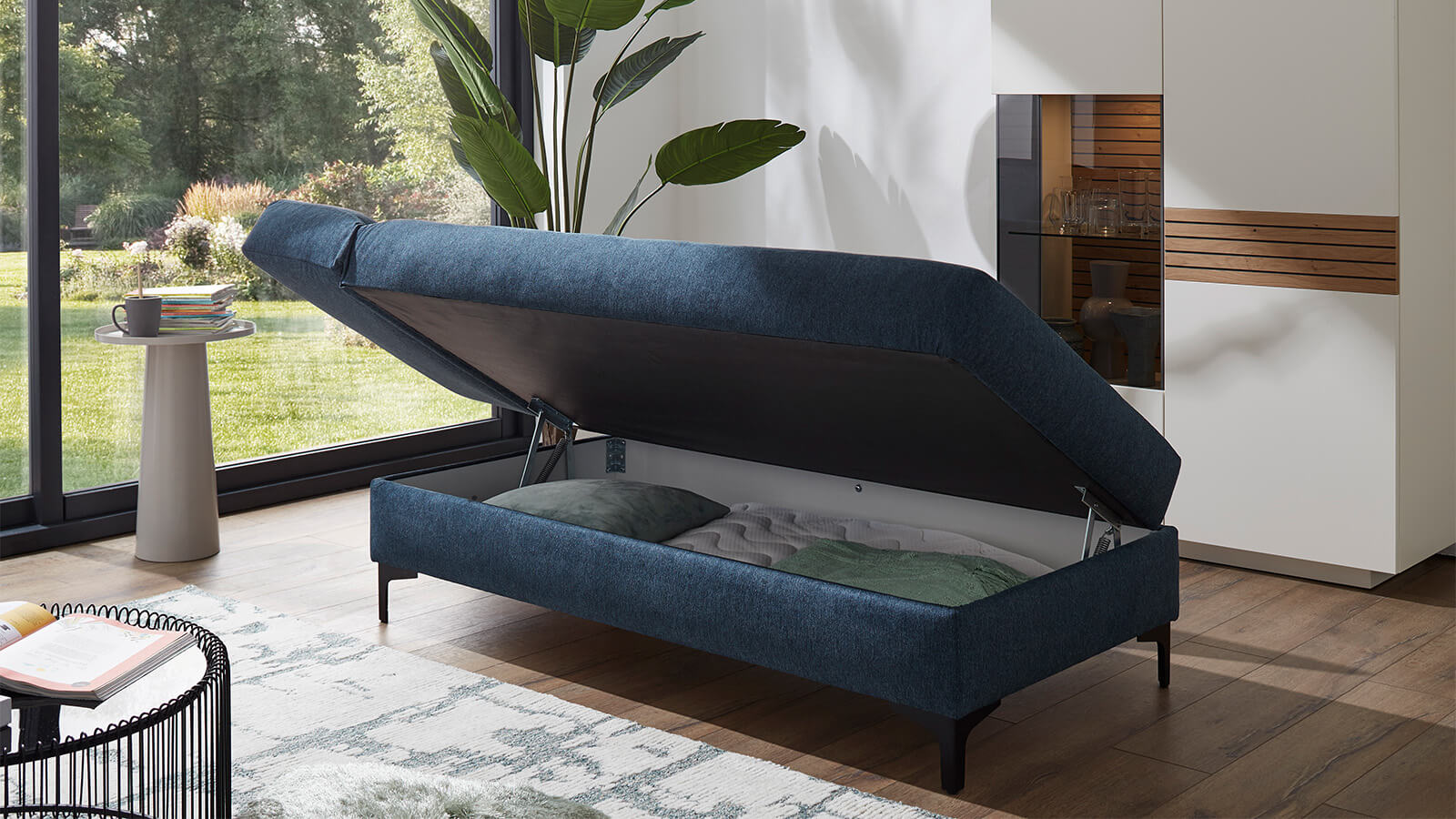 Großzügiges Schlafsofa mit Stoffbezug in verschiedenen Farben, komfortabler Sitzfläche, breiten Armlehnen, zwei Rückenkissen und schwarzen Designfüßen aus Metall