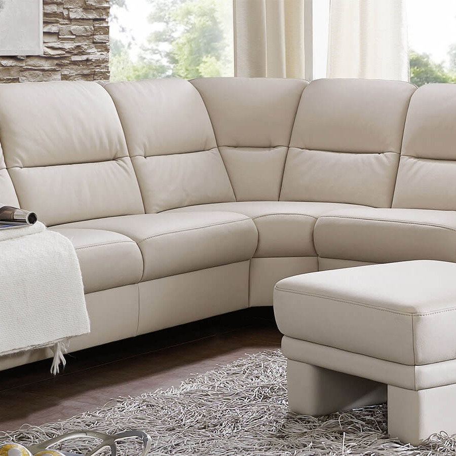 Große beige Wohnlandschaft mit großzügiger Sitzfläche, gepolsterten Rückenlehnen und passendem Hocker in einem hellen Wohnzimmer