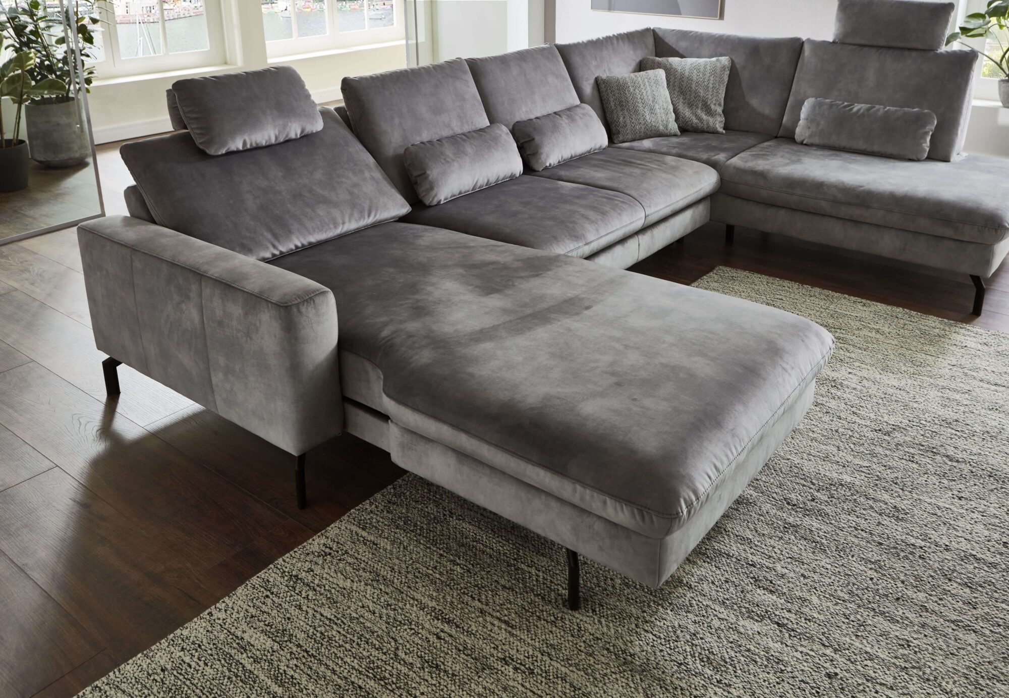 Wohnlandschaft in Silbergrau aus weichem Velour mit Longchair, schwarzem Metallgestell und großzügiger Eckform als gemütlicher Mittelpunkt im Wohnzimmer