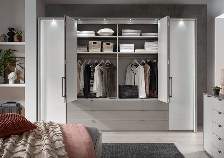 Offener Kleiderschrank des Schlafzimmerprogramms &bdquo;Marbella&ldquo; mit grauen Lackfronten und wei&szlig;en Glaseins&auml;tzen.