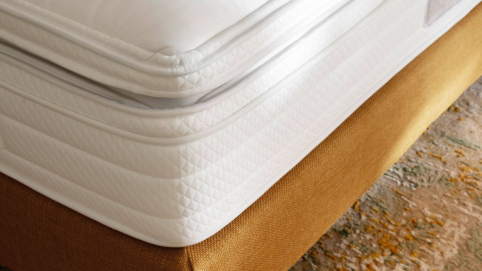Boxspringbett Navelli von Contur mit hohem, gepolstertem Kopfteil, edlem Stoffbezug in Grau oder Kurkuma und großzügiger Liegefläche als stilvoller Mittelpunkt eines modernen Schlafzimmers.