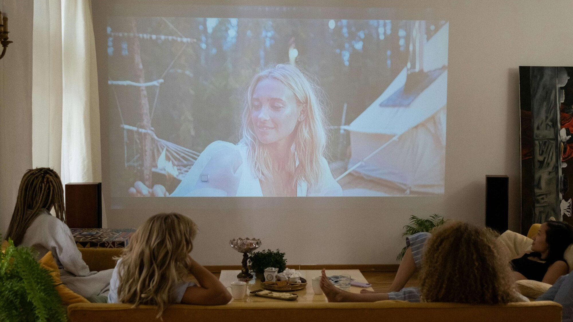 Mehrere Personen sitzen entspannt auf einer Couch und schauen einen Film, der mit einem Beamer an die Wand projiziert wird.