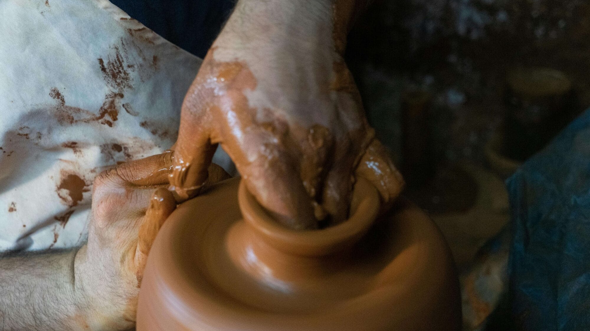 Nahaufnahme von Händen beim Formen eines Tongefäßes auf der Töpferscheibe – Symbol für traditionelles Handwerk und organisches Wohndesign.