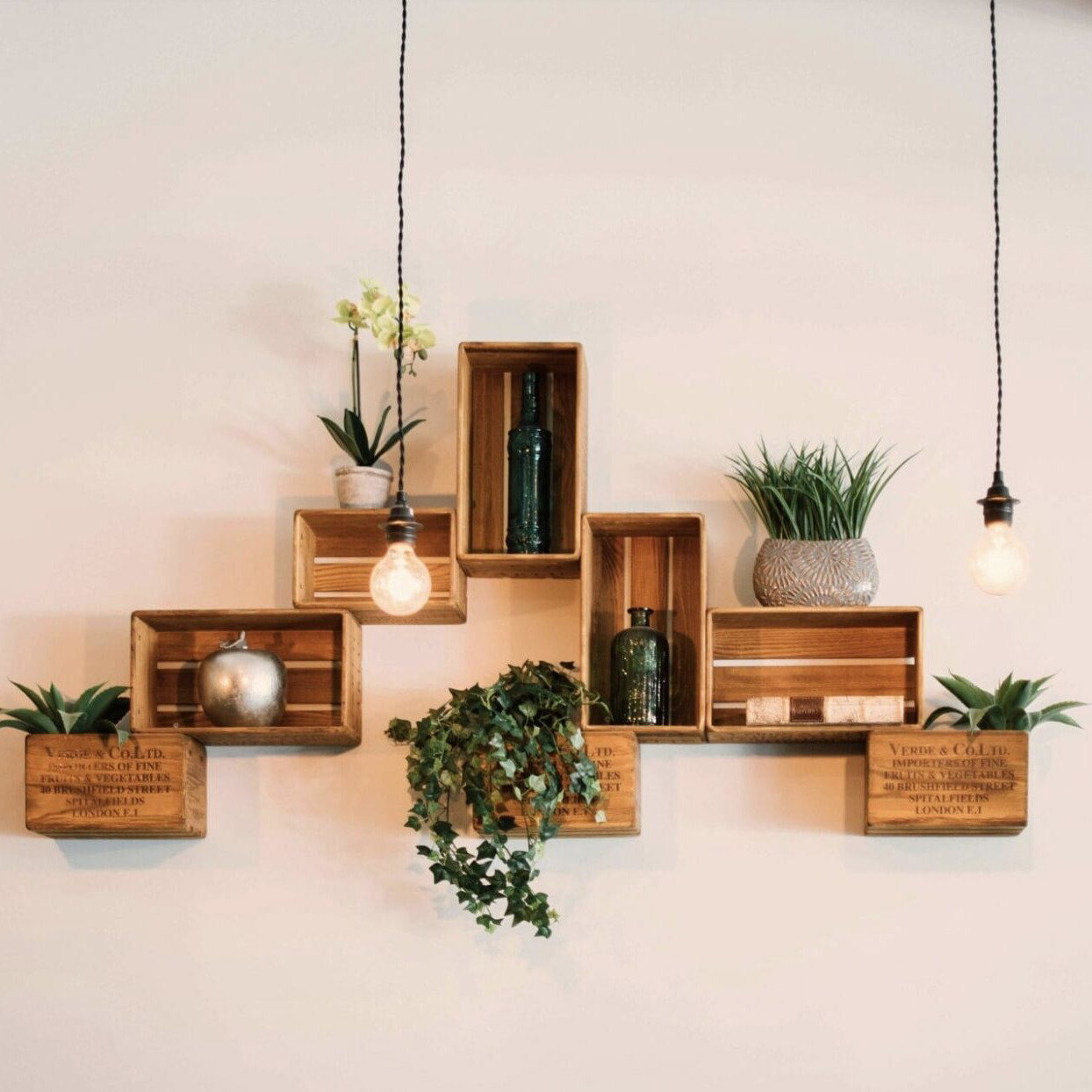 Wanddekoration aus Holzkisten mit Pflanzen, Glasvasen und Hängeleuchten – kreatives Interior Design als Ausdruck individueller Persönlichkeit.