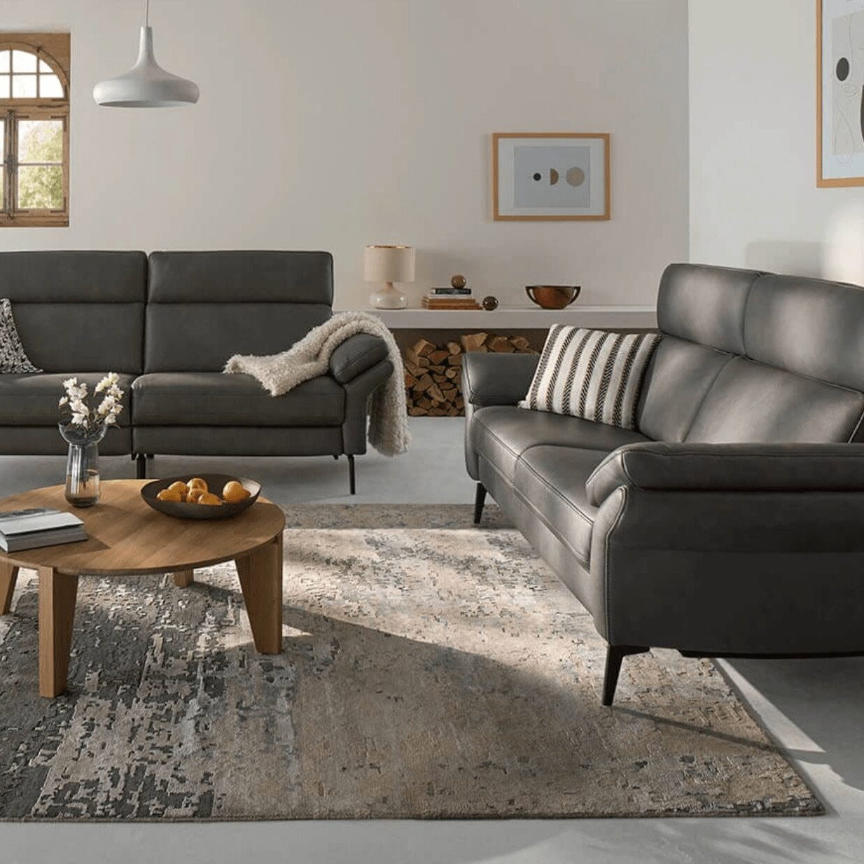 Modernes Wohnzimmer mit zwei dunkelgrauen Ledersofas und rundem Holzcouchtisch.
