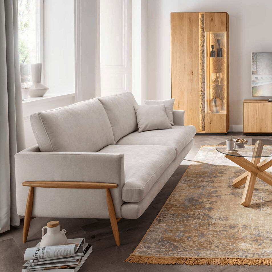 Helles Sofa mit Holzarmlehnen in einem modernen Wohnzimmer mit Massivholzmöbeln.Beim Wohnung einrichten bilden ein komfortables Sofa und natürliche Materialien die Grundlage für ein harmonisches Zuhause. Helle Farben lassen Wohnräume freundlich und offen wirken.