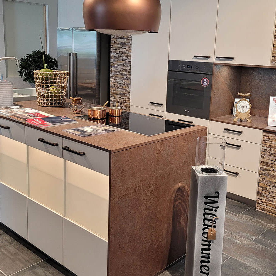 Ausstellungsküche mit seidengrauen Fronten, dunkler Arbeitsfläche, Kücheninsel, Keramikspüle und Elektrogeräten von Miele, Liebherr und Falmec.