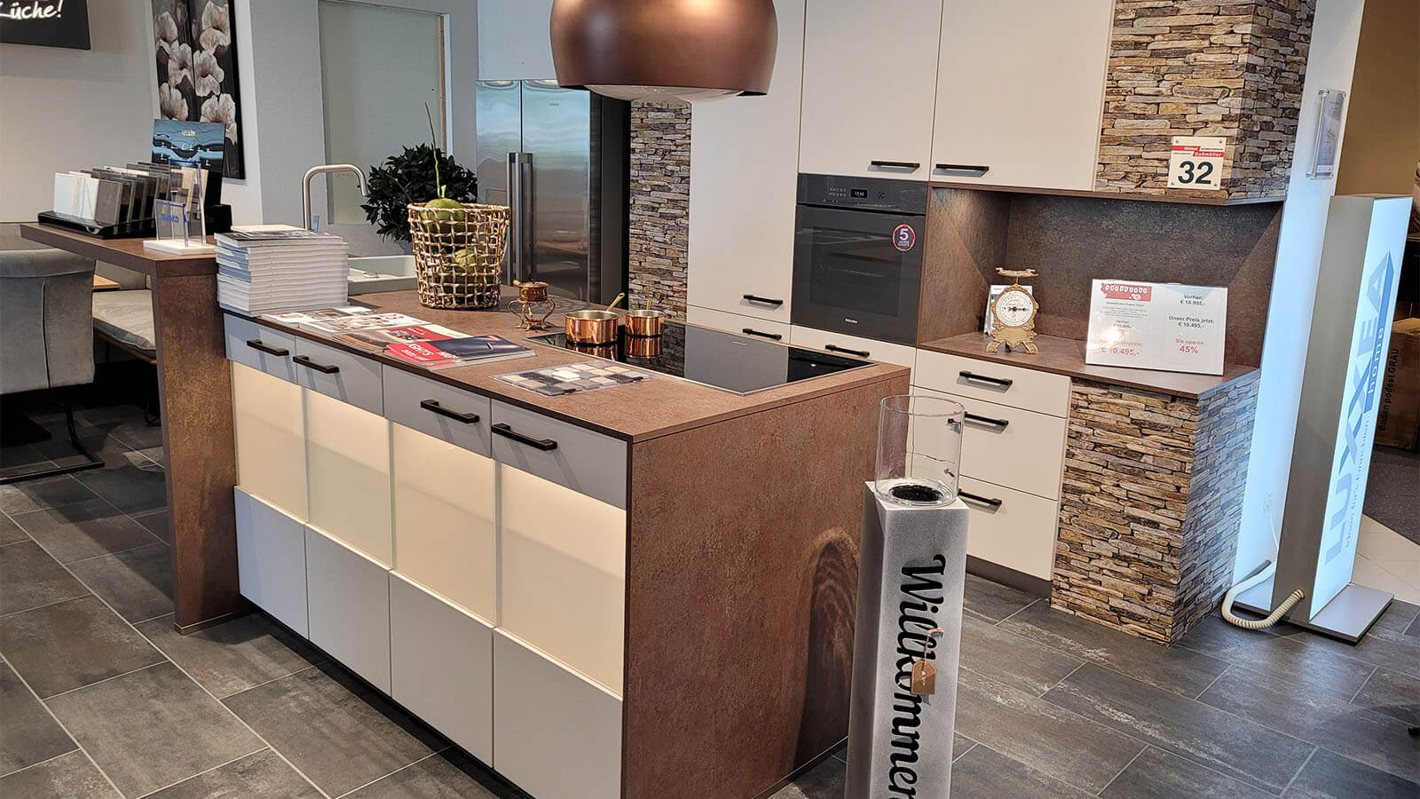 Ausstellungsküche mit seidengrauen Fronten, dunkler Arbeitsfläche, Kücheninsel, Keramikspüle und Elektrogeräten von Miele, Liebherr und Falmec.
