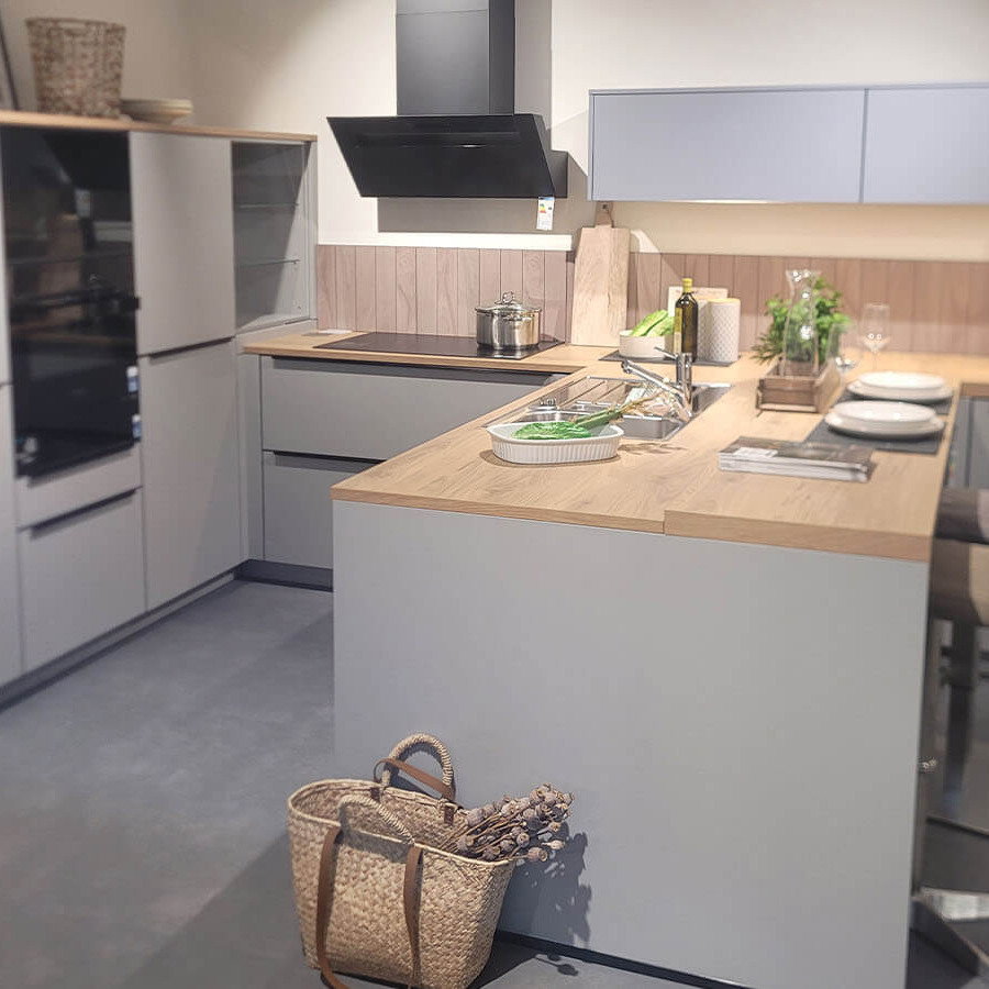 Großzügige Ausstellungsküche in Steingrau mit Arbeitsplatte in Holzoptik, Halbinsel, Sitzbereich und Elektrogeräten von Siemens und Liebherr.