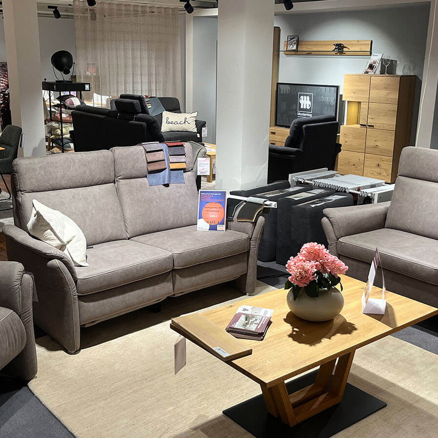 Elegante Wohnlandschaft in Bulus Stone mit weicher Stoffoberfläche, beiger Kontrastnaht, breiten Sitzelementen, niedrigen Armlehnen, Aluminiumfüßen und elektrischem Relaxsessel