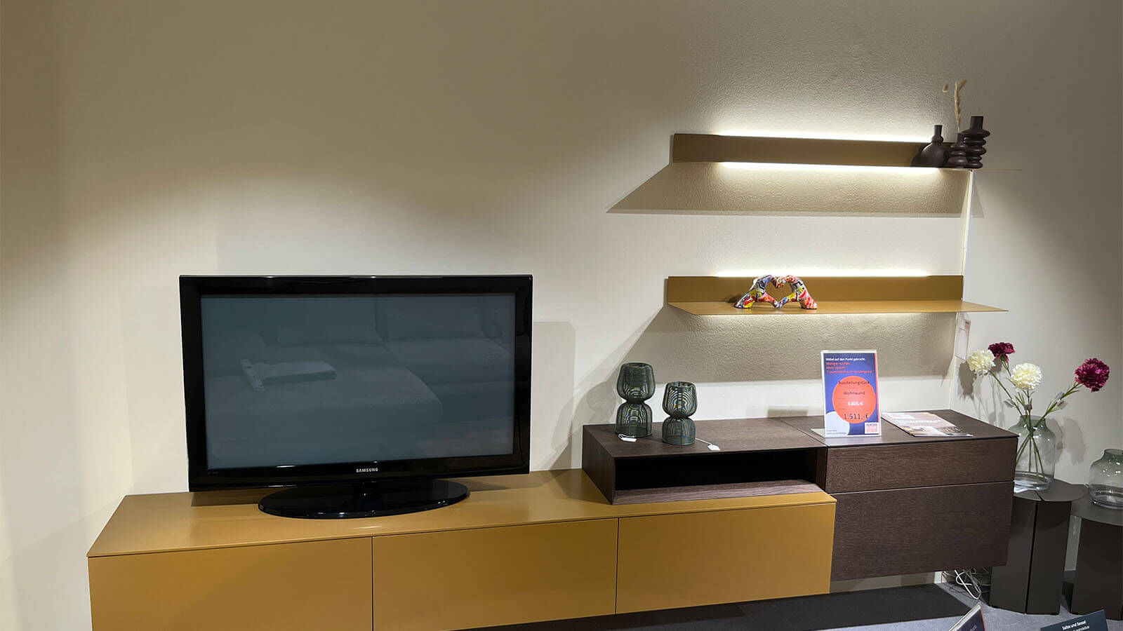 Wandhängende Wohnwand in Lack Amber matt mit schwebendem Lowboard, natürlichem Rovere-Terra-Aufsatzelement, grifflosen Fronten mit Push-to-open und rückseitig beleuchtetem LED-Wandboard für eine warme Wohnatmosphäre