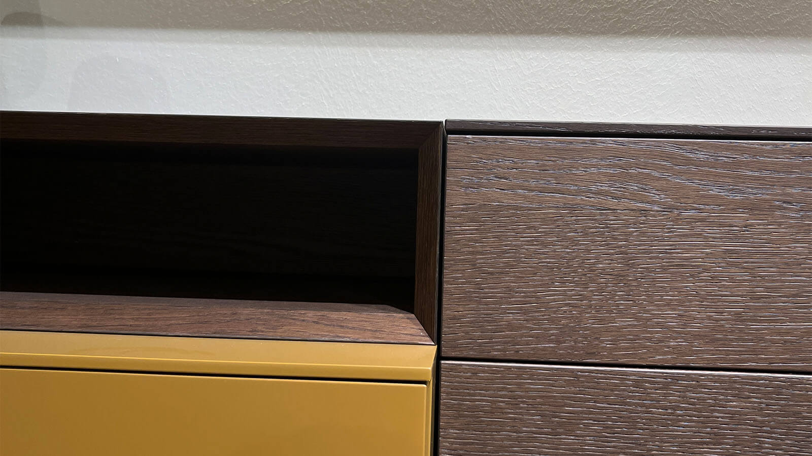 Wandhängende Wohnwand in Lack Amber matt mit schwebendem Lowboard, natürlichem Rovere-Terra-Aufsatzelement, grifflosen Fronten mit Push-to-open und rückseitig beleuchtetem LED-Wandboard für eine warme Wohnatmosphäre