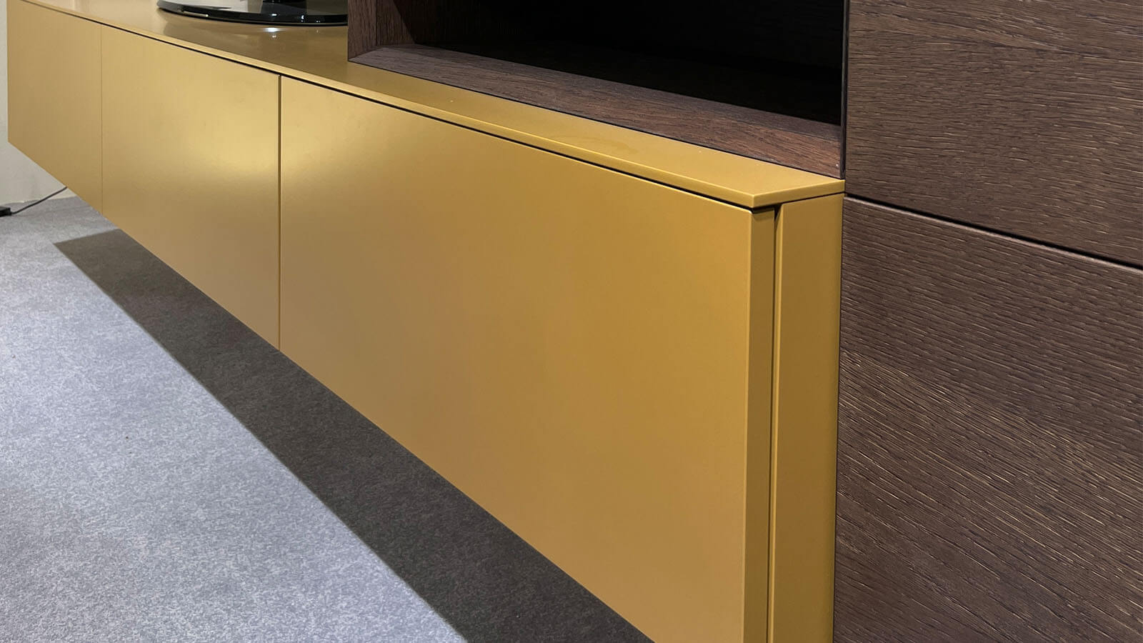 Wandhängende Wohnwand in Lack Amber matt mit schwebendem Lowboard, natürlichem Rovere-Terra-Aufsatzelement, grifflosen Fronten mit Push-to-open und rückseitig beleuchtetem LED-Wandboard für eine warme Wohnatmosphäre