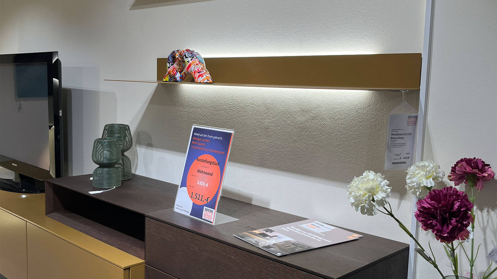 Wandhängende Wohnwand in Lack Amber matt mit schwebendem Lowboard, natürlichem Rovere-Terra-Aufsatzelement, grifflosen Fronten mit Push-to-open und rückseitig beleuchtetem LED-Wandboard für eine warme Wohnatmosphäre