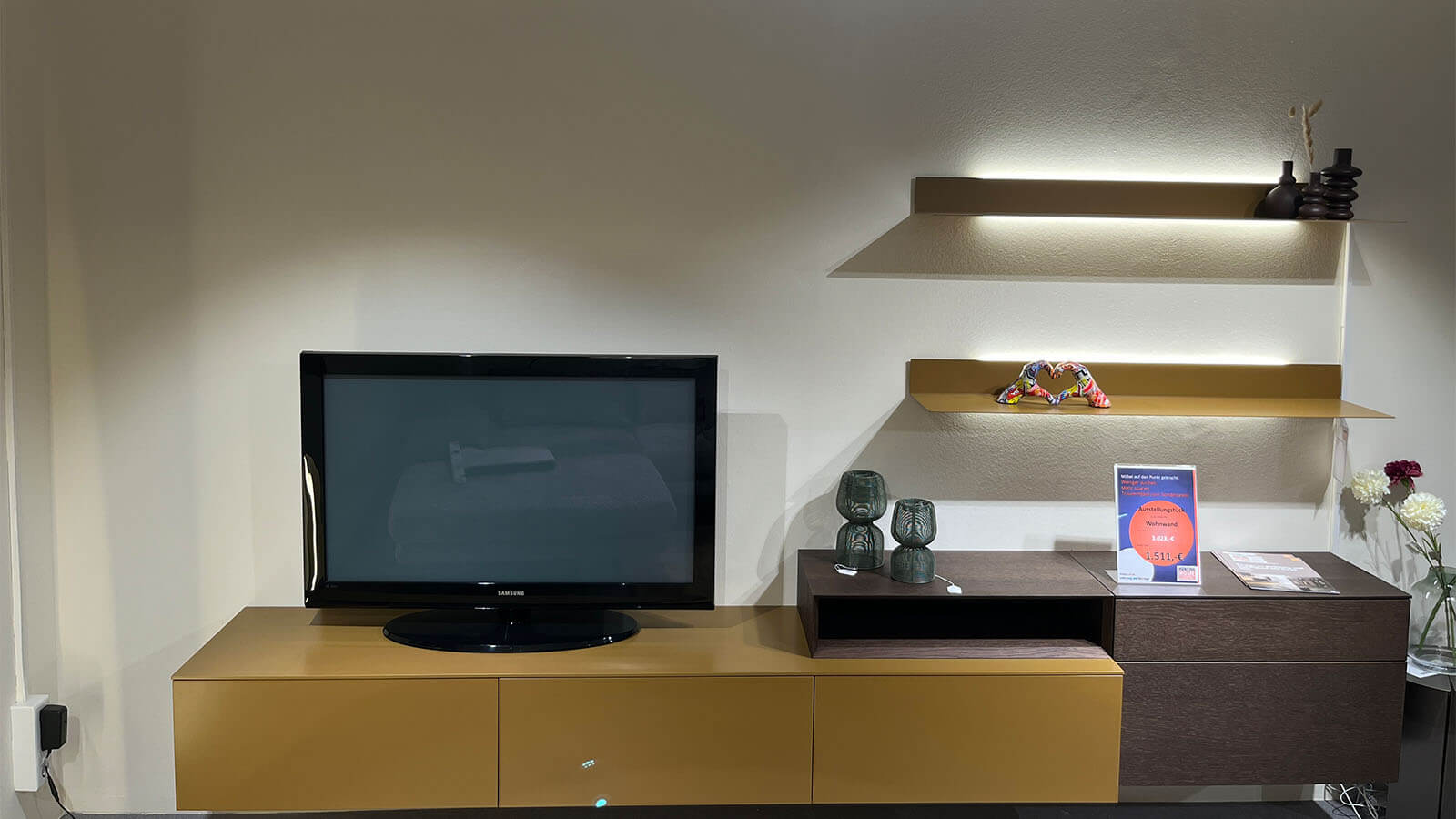 Wandhängende Wohnwand in Lack Amber matt mit schwebendem Lowboard, natürlichem Rovere-Terra-Aufsatzelement, grifflosen Fronten mit Push-to-open und rückseitig beleuchtetem LED-Wandboard für eine warme Wohnatmosphäre