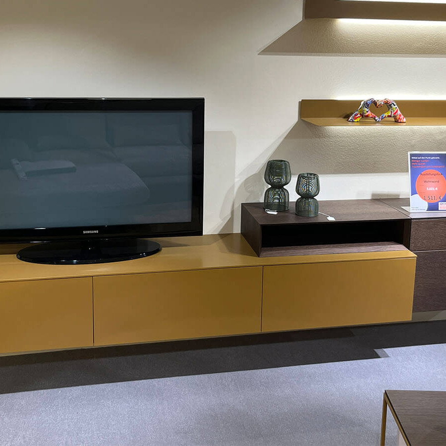 Wandhängende Wohnwand in Lack Amber matt mit schwebendem Lowboard, natürlichem Rovere-Terra-Aufsatzelement, grifflosen Fronten mit Push-to-open und rückseitig beleuchtetem LED-Wandboard für eine warme Wohnatmosphäre