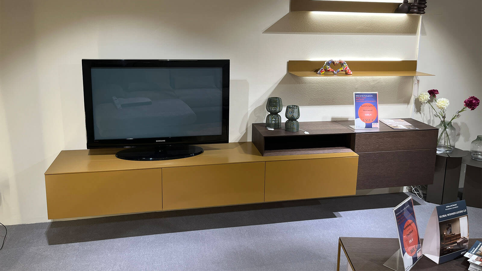 Wandhängende Wohnwand in Lack Amber matt mit schwebendem Lowboard, natürlichem Rovere-Terra-Aufsatzelement, grifflosen Fronten mit Push-to-open und rückseitig beleuchtetem LED-Wandboard für eine warme Wohnatmosphäre