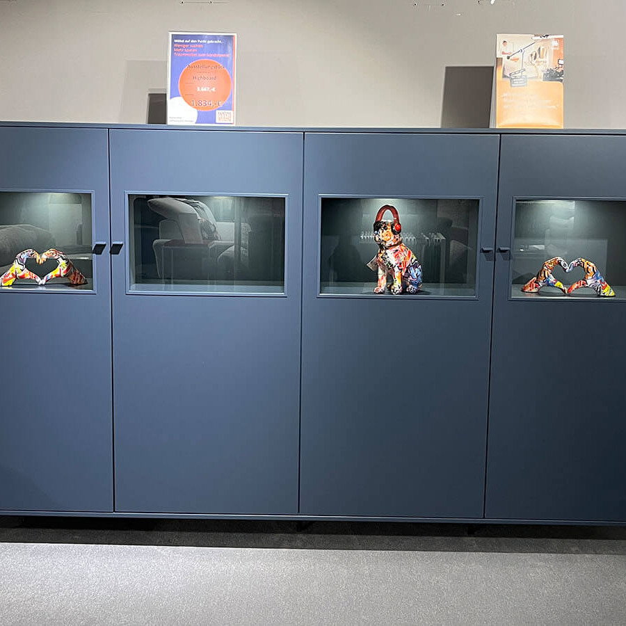 Breites Highboard in Atlantikblau mit hochwertiger Lackoberfläche, vier gleichmäßig angeordneten Frontsegmenten, farbgleichen Griffen und filigranem Kufengestell für eine klare, geradlinige Wohnraumgestaltung.
