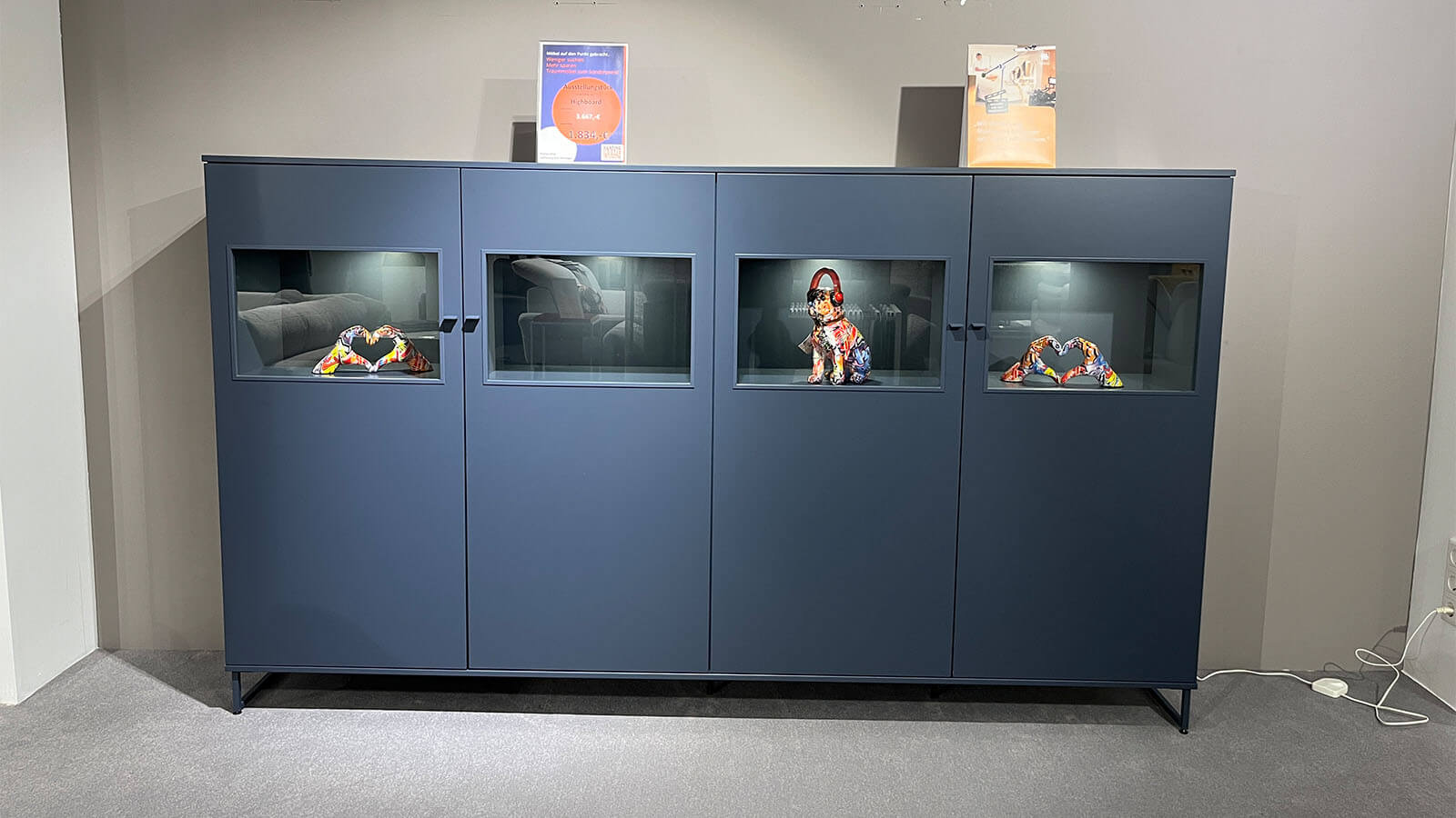 Breites Highboard in Atlantikblau mit hochwertiger Lackoberfläche, vier gleichmäßig angeordneten Frontsegmenten, farbgleichen Griffen und filigranem Kufengestell für eine klare, geradlinige Wohnraumgestaltung.
