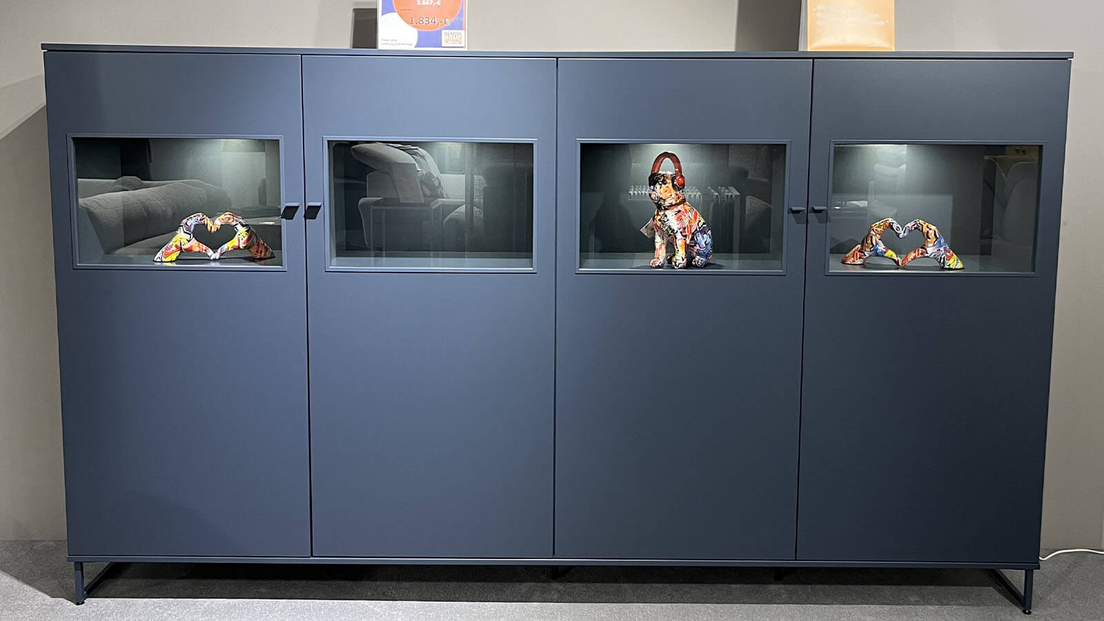 Breites Highboard in Atlantikblau mit hochwertiger Lackoberfläche, vier gleichmäßig angeordneten Frontsegmenten, farbgleichen Griffen und filigranem Kufengestell für eine klare, geradlinige Wohnraumgestaltung.