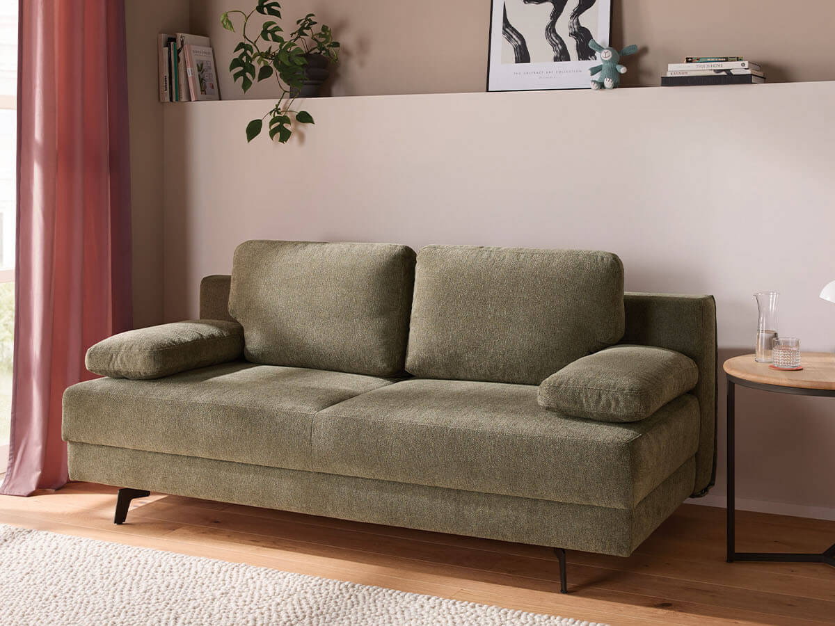 Großzügiges grünes Schlafsofa mit weichem Stoffbezug, lässiger Polsterung und gemütlichen Armlehnenkissen. Die schwarzen Metallfüße setzen einen modernen Akzent, während der integrierte Bettkasten praktischen Stauraum bietet.