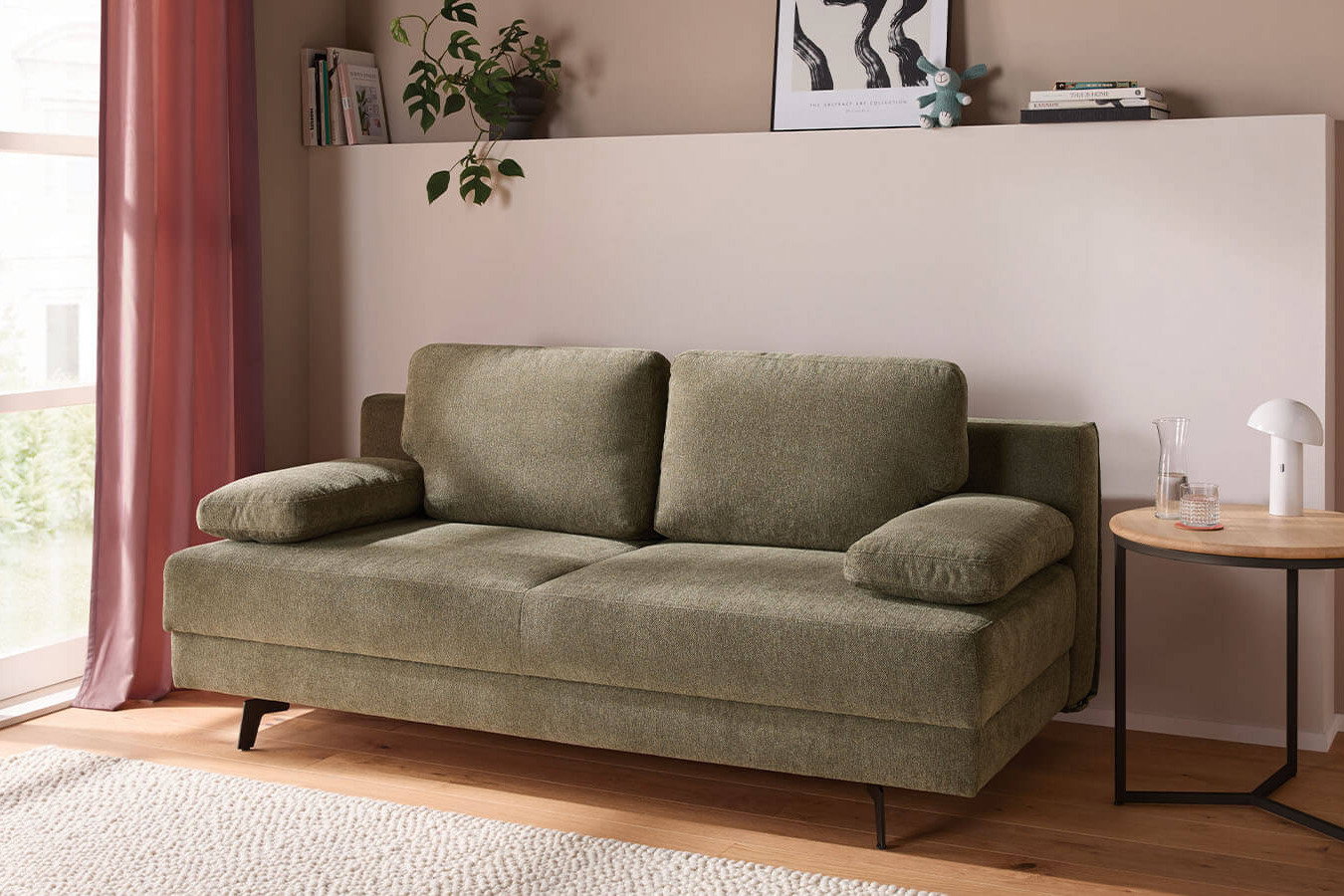 Großzügiges grünes Schlafsofa mit weichem Stoffbezug, lässiger Polsterung und gemütlichen Armlehnenkissen. Die schwarzen Metallfüße setzen einen modernen Akzent, während der integrierte Bettkasten praktischen Stauraum bietet.