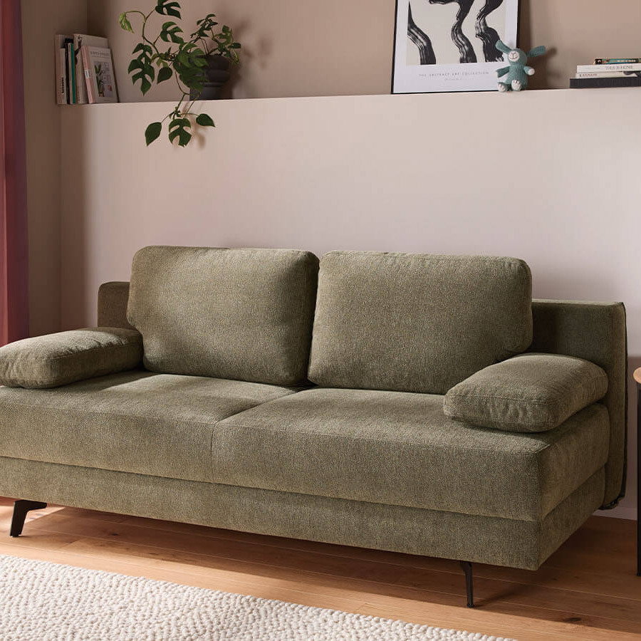 Großzügiges grünes Schlafsofa mit weichem Stoffbezug, lässiger Polsterung und gemütlichen Armlehnenkissen. Die schwarzen Metallfüße setzen einen modernen Akzent, während der integrierte Bettkasten praktischen Stauraum bietet.
