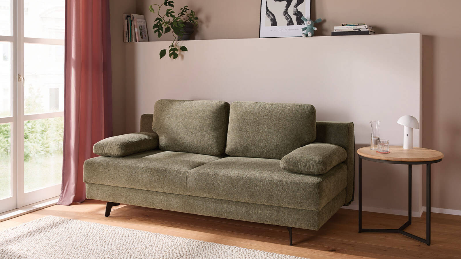 Großzügiges grünes Schlafsofa mit weichem Stoffbezug, lässiger Polsterung und gemütlichen Armlehnenkissen. Die schwarzen Metallfüße setzen einen modernen Akzent, während der integrierte Bettkasten praktischen Stauraum bietet.