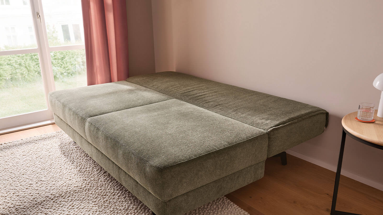 Großzügiges grünes Schlafsofa mit weichem Stoffbezug, lässiger Polsterung und gemütlichen Armlehnenkissen. Die schwarzen Metallfüße setzen einen modernen Akzent, während der integrierte Bettkasten praktischen Stauraum bietet.