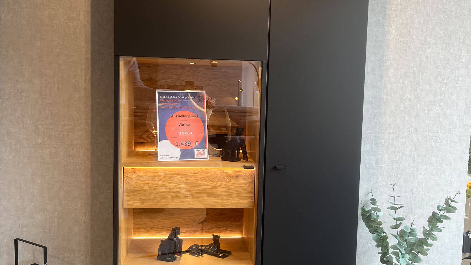 Hohe Vitrine in mattem Anthrazit mit grifflosen Türen, Akzenten aus geölter Massivholz-Eiche und stimmungsvoller Innenbeleuchtung