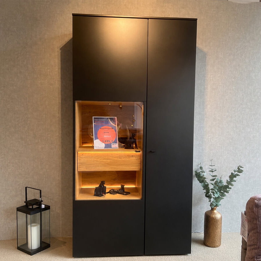 Hohe Vitrine in mattem Anthrazit mit grifflosen Türen, Akzenten aus geölter Massivholz-Eiche und stimmungsvoller Innenbeleuchtung