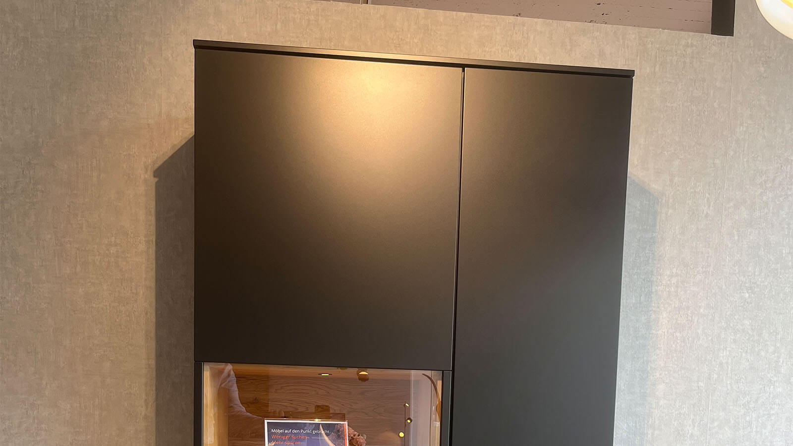 Hohe Vitrine in mattem Anthrazit mit grifflosen Türen, Akzenten aus geölter Massivholz-Eiche und stimmungsvoller Innenbeleuchtung