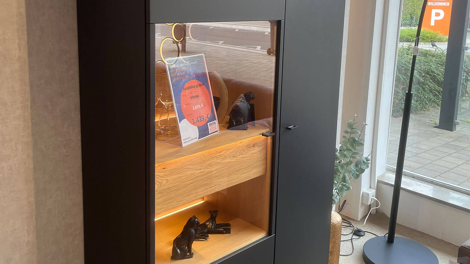 Hohe Vitrine in mattem Anthrazit mit grifflosen Türen, Akzenten aus geölter Massivholz-Eiche und stimmungsvoller Innenbeleuchtung