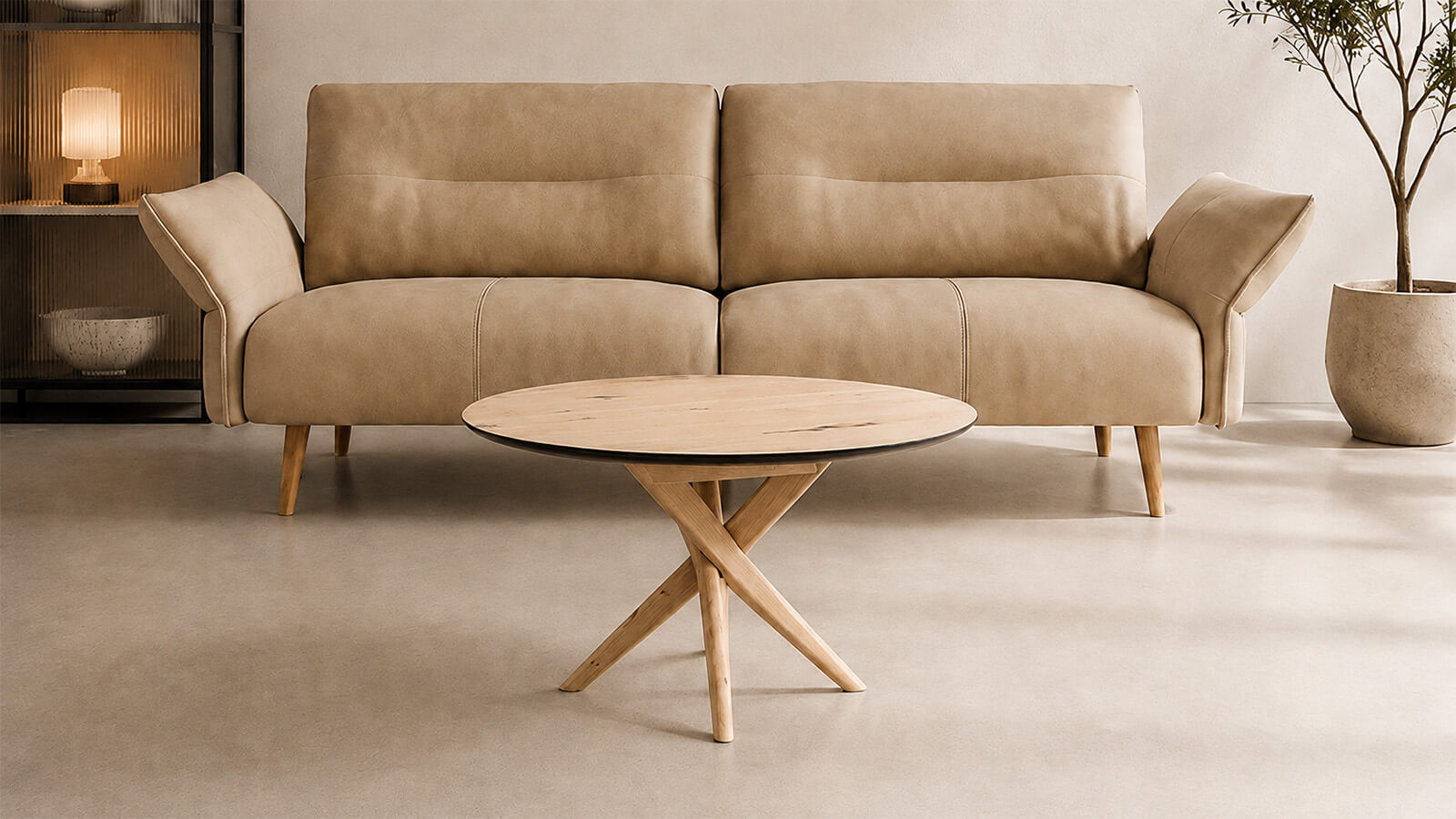 Ein runder Couchtisch aus hellem Holz von Jakobsen Copenhagen steht als eleganter Mittelpunkt vor einem beigen Designsofa. Das warme Tageslicht unterstreicht die natürliche Holzmaserung, während eine moderne Vitrine mit indirekter Beleuchtung und eine stilvolle Zimmerpflanze eine ruhige, skandinavische Wohnatmosphäre schaffen.