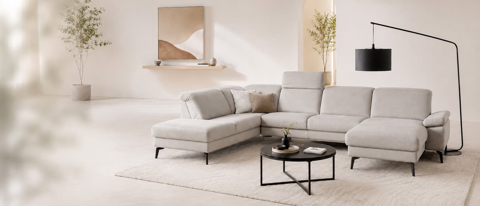 Helles, modernes Wohnzimmer mit großer hellgrauer Wohnlandschaft, schwarzem Couchtisch und minimalistischer Stehleuchte in warmen Beigetönen.