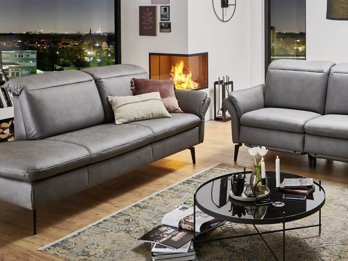 Modern Classic FU Sofa von Gruber in einem eleganten Wohnambiente mit gro&szlig;z&uuml;giger Sitzlandschaft, weichen Polstern und klaren Linien. Das Sofa steht im Mittelpunkt eines stilvoll eingerichteten Raumes.